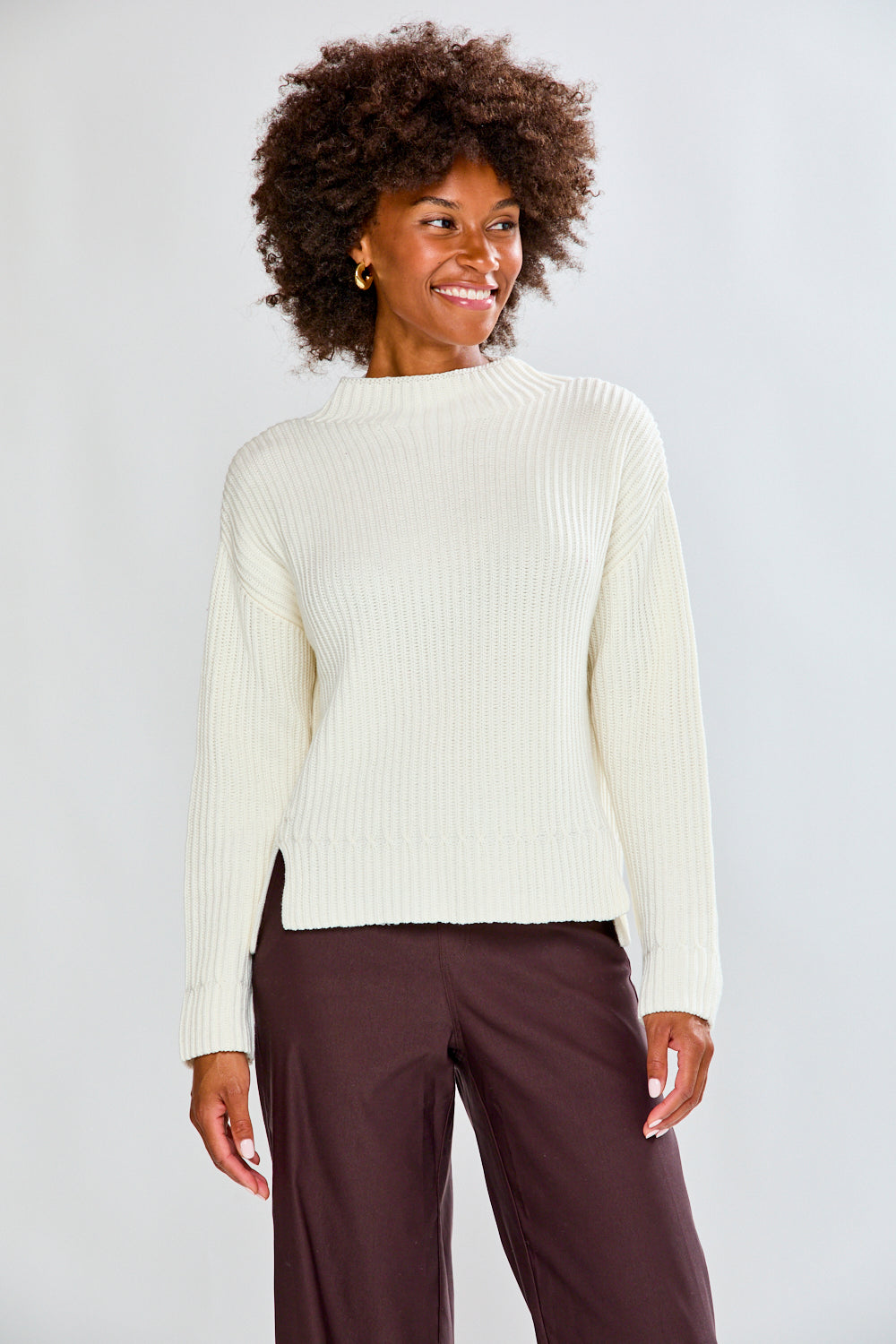 Woman wearing a ivory ribbed sweater and white pants on a plain background