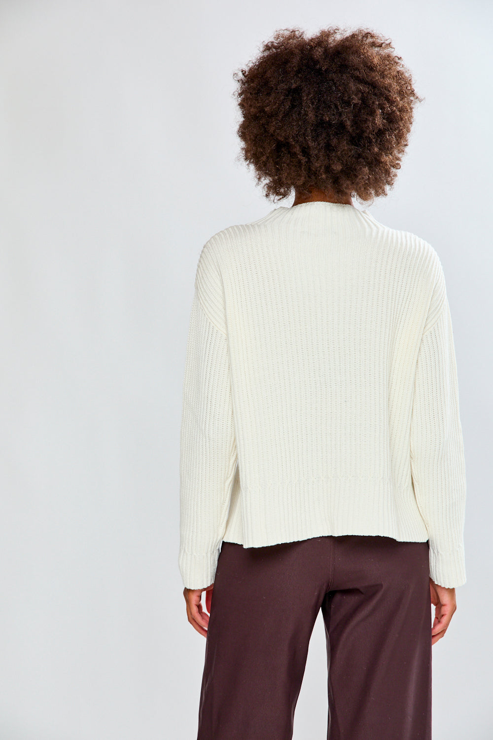 Woman wearing a ivory ribbed sweater and white pants on a plain background