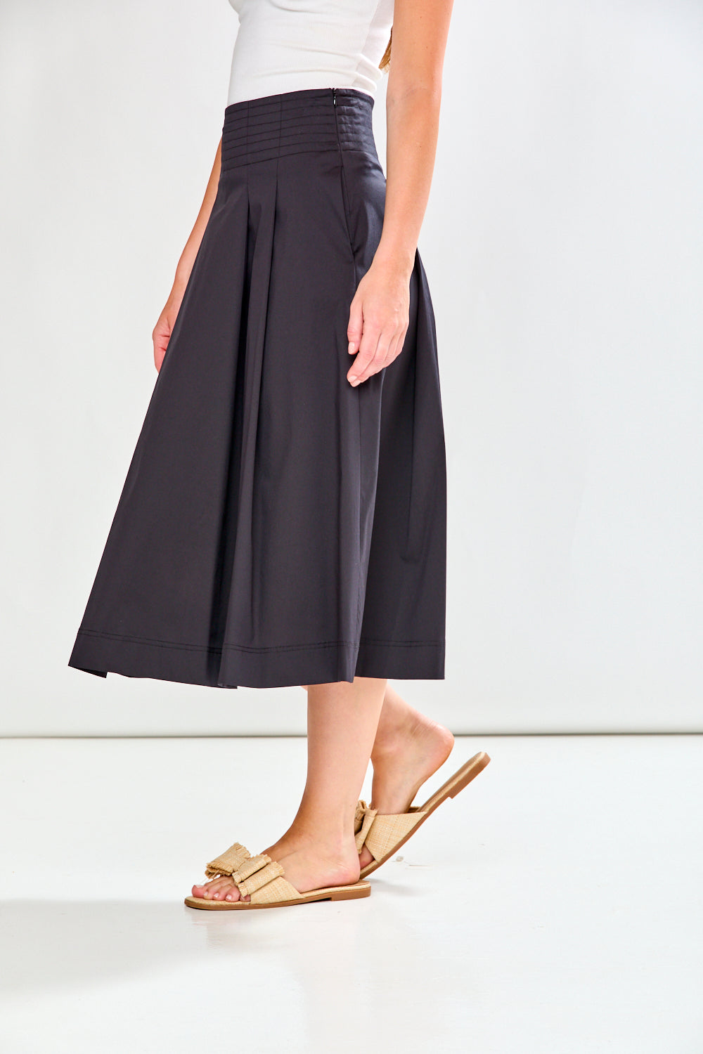 Person wearing a black skirt and beige sandals on a white background