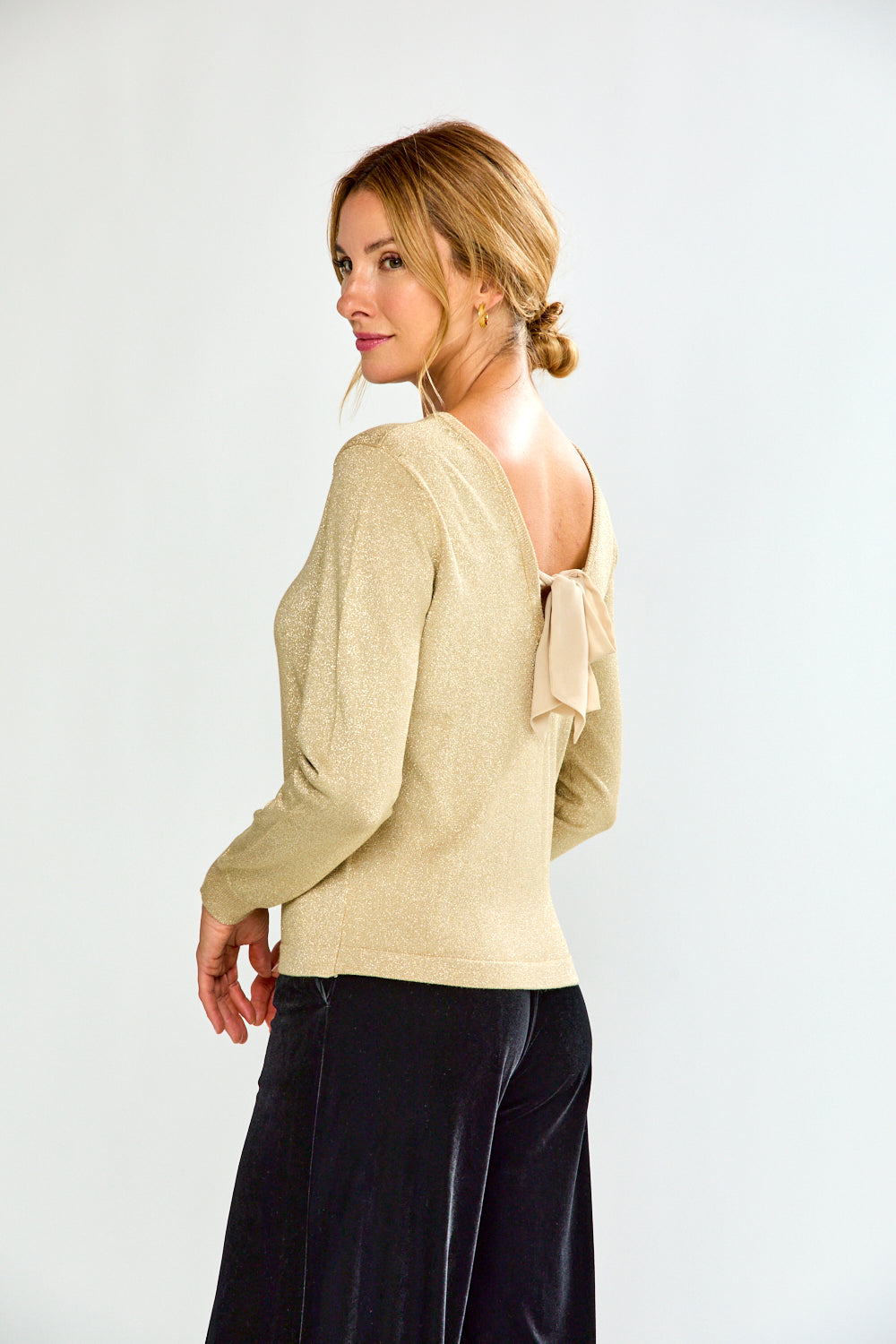 Woman wearing a gold sweater and black pants on a white background