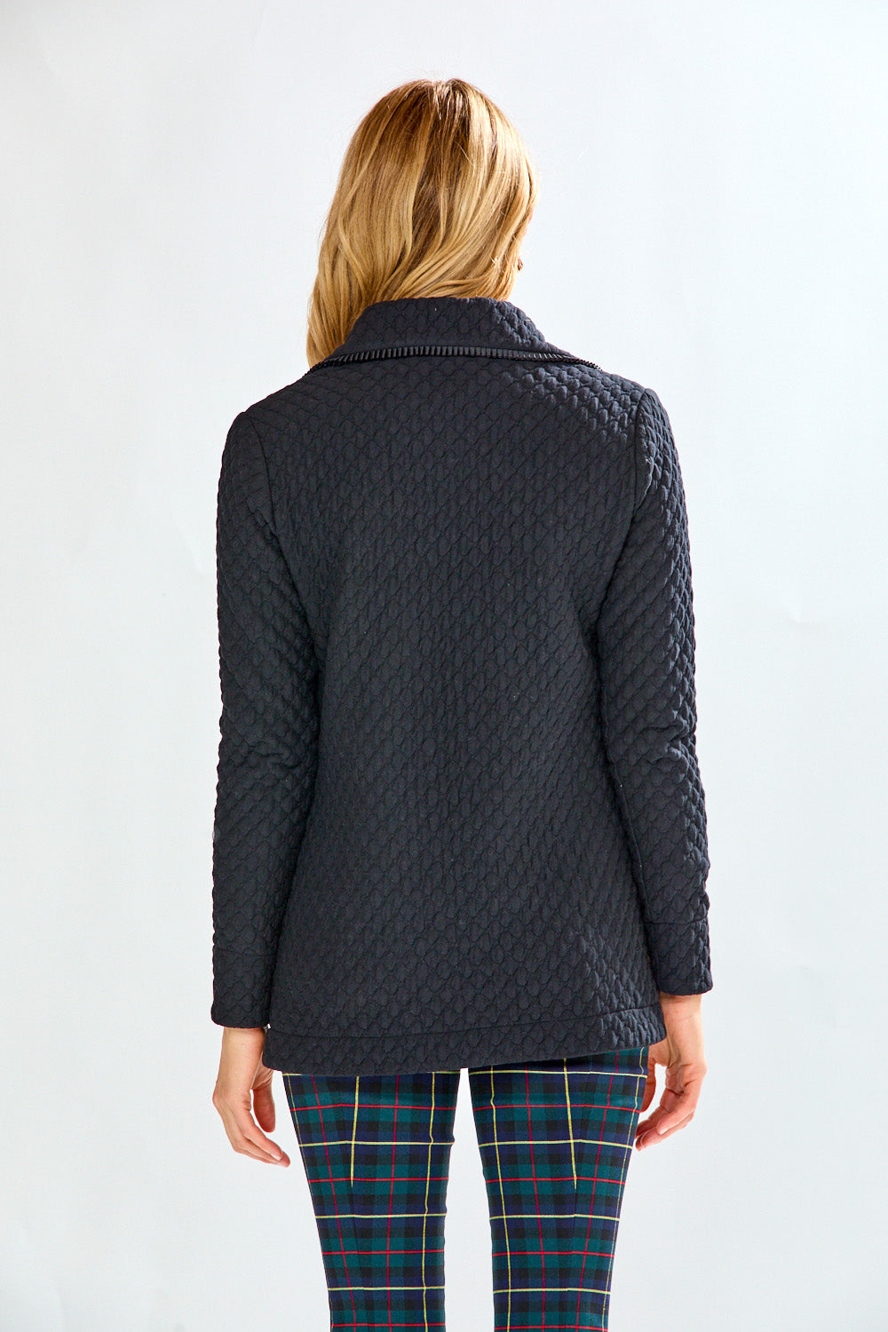 Woman wearing a black quilted jacket and plaid pants on a white background