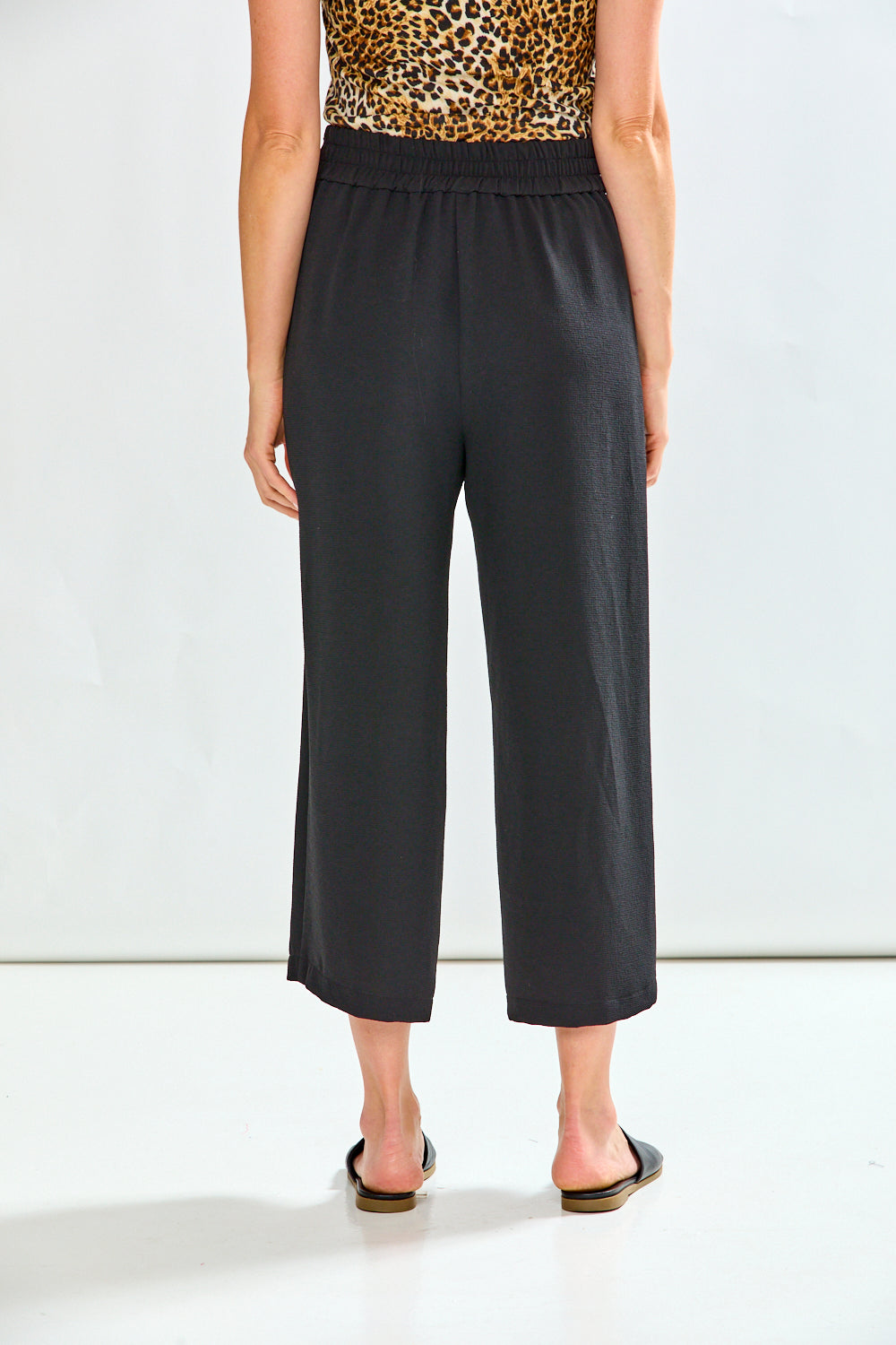 Person wearing black wide-leg pants with a leopard print top on a white background