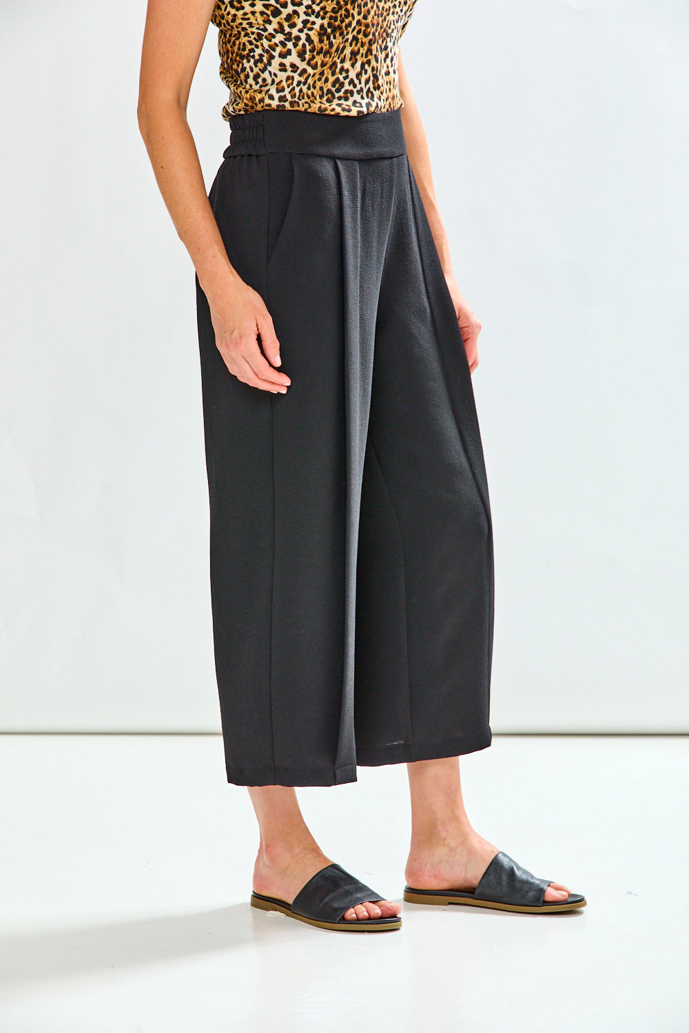 Person wearing black wide-leg pants with a leopard print top on a white background