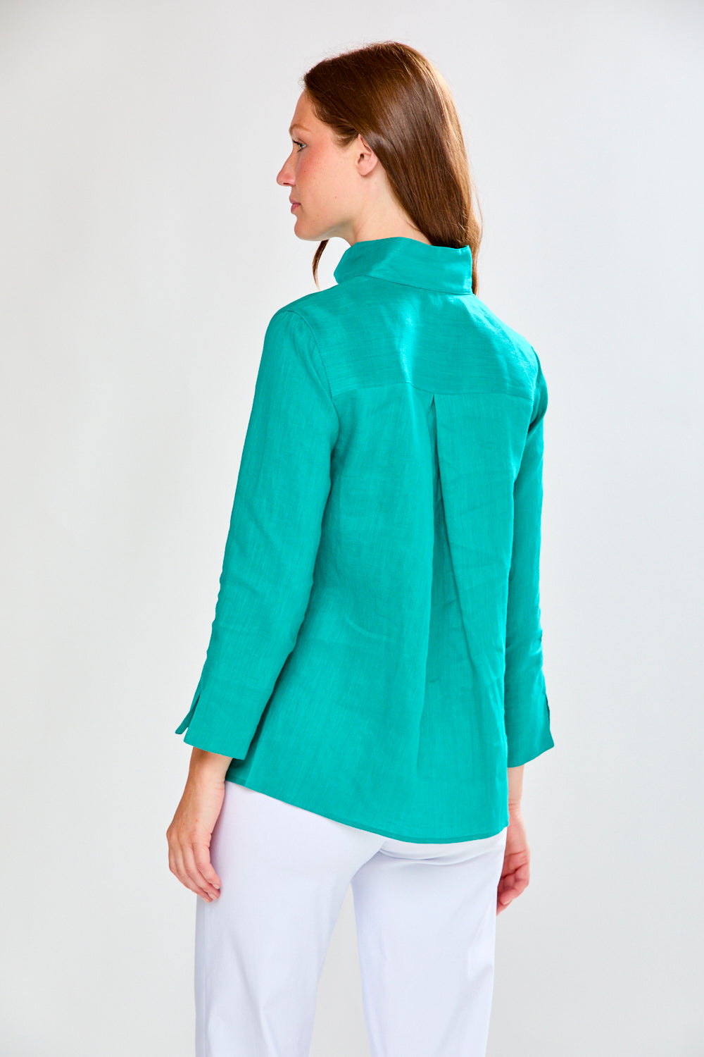 Woman wearing a teal jacket and white pants on a plain background