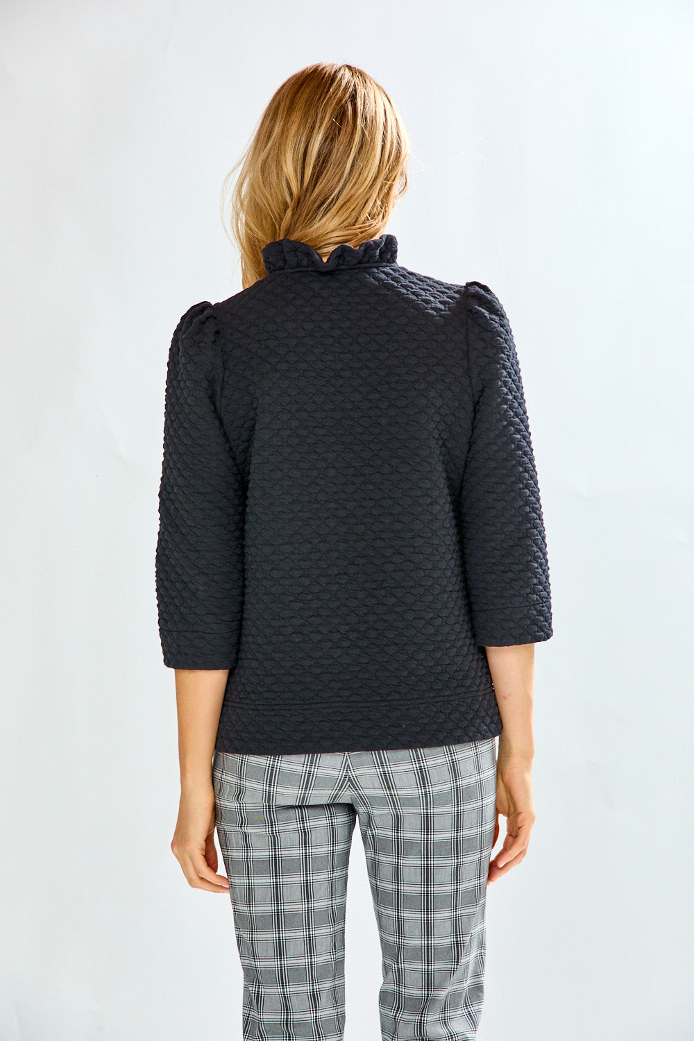 Woman wearing a textured black sweater and plaid pants against a light background