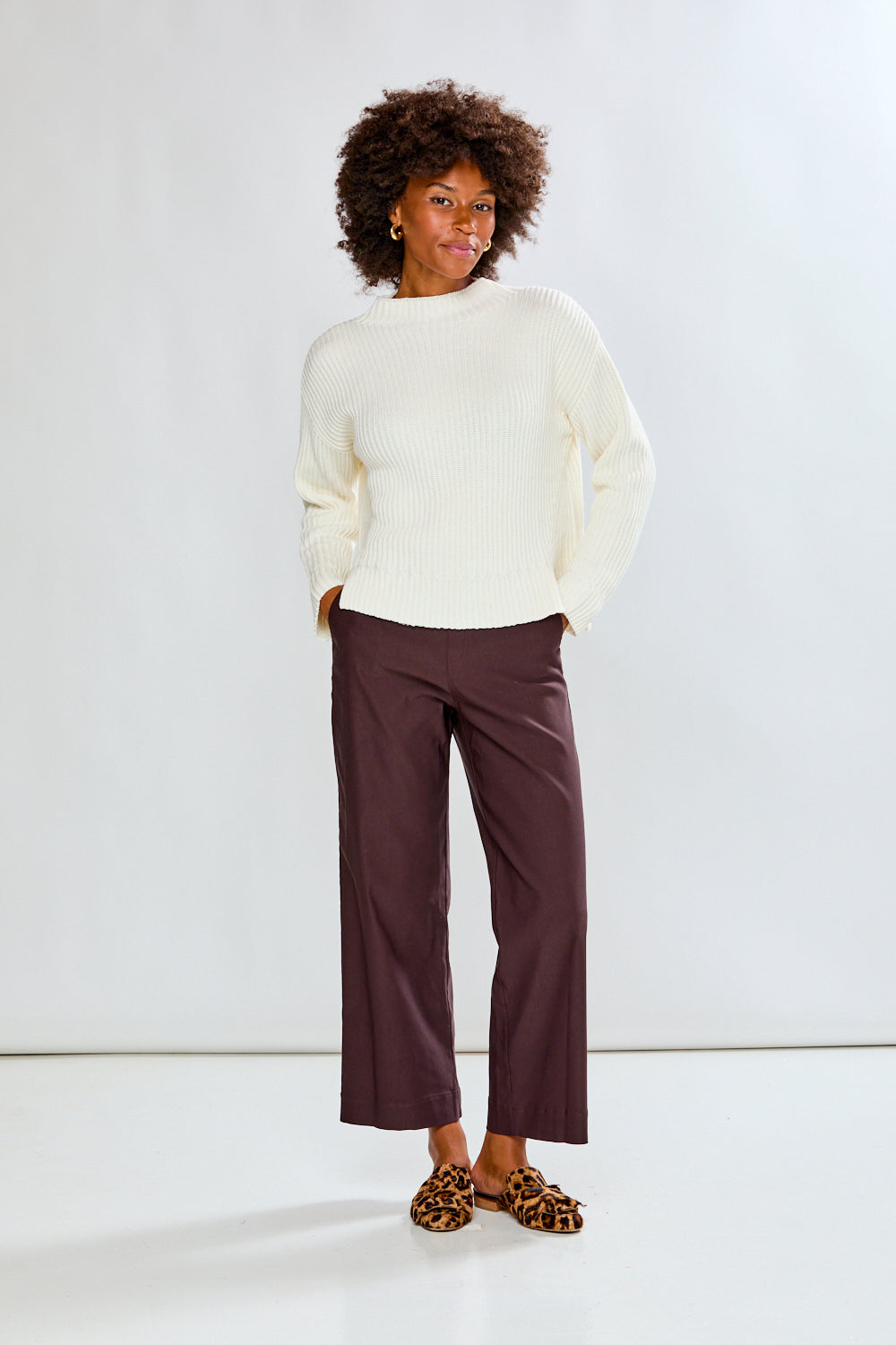 Woman wearing a ivory ribbed sweater and white pants on a plain background
