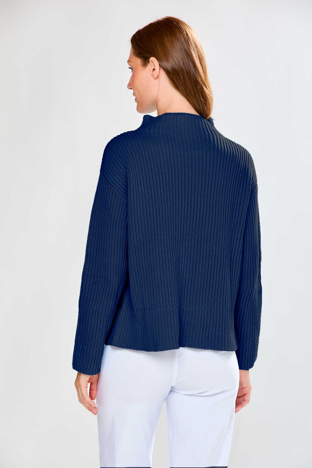 Woman wearing a navy ribbed sweater and white pants on a plain background