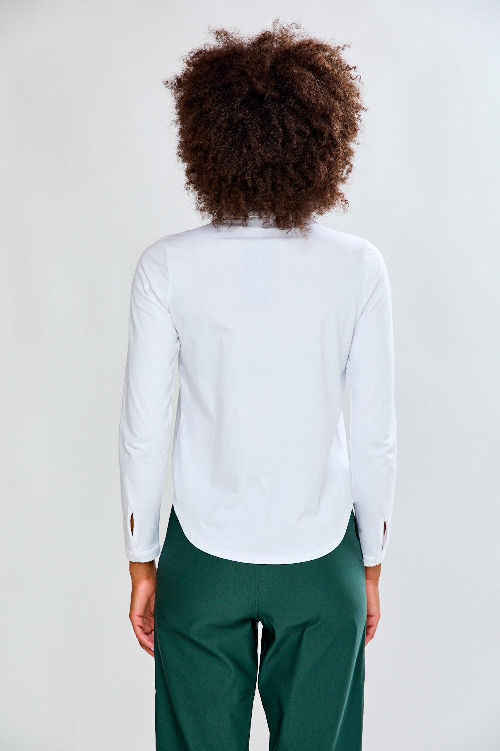 Woman wearing a white shirt and green pants against a plain background