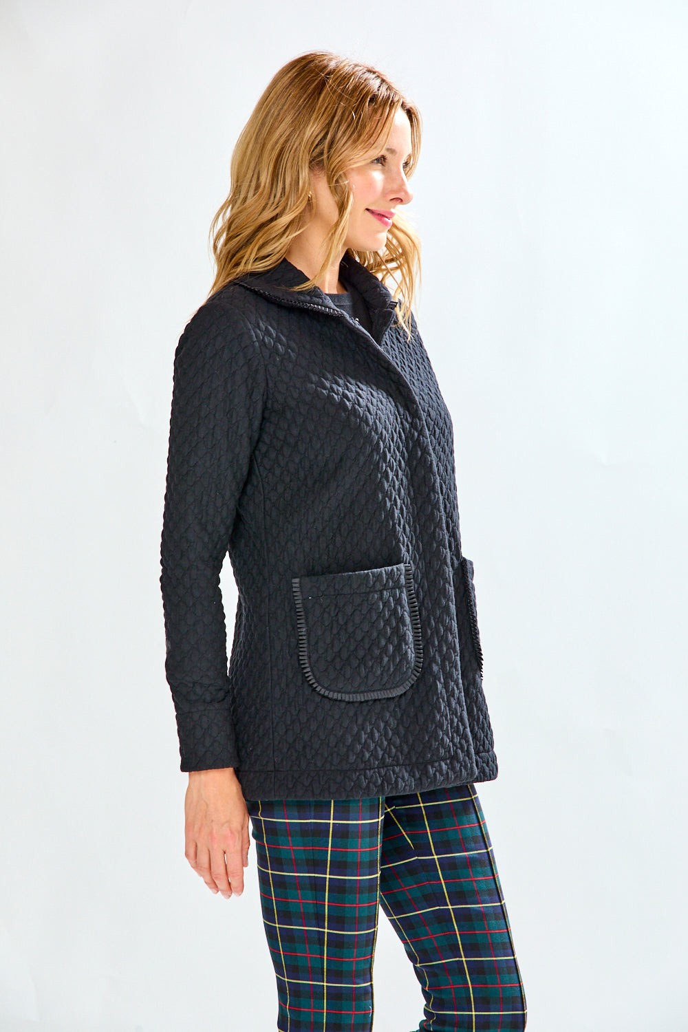 Woman wearing a black quilted jacket and plaid pants on a white background