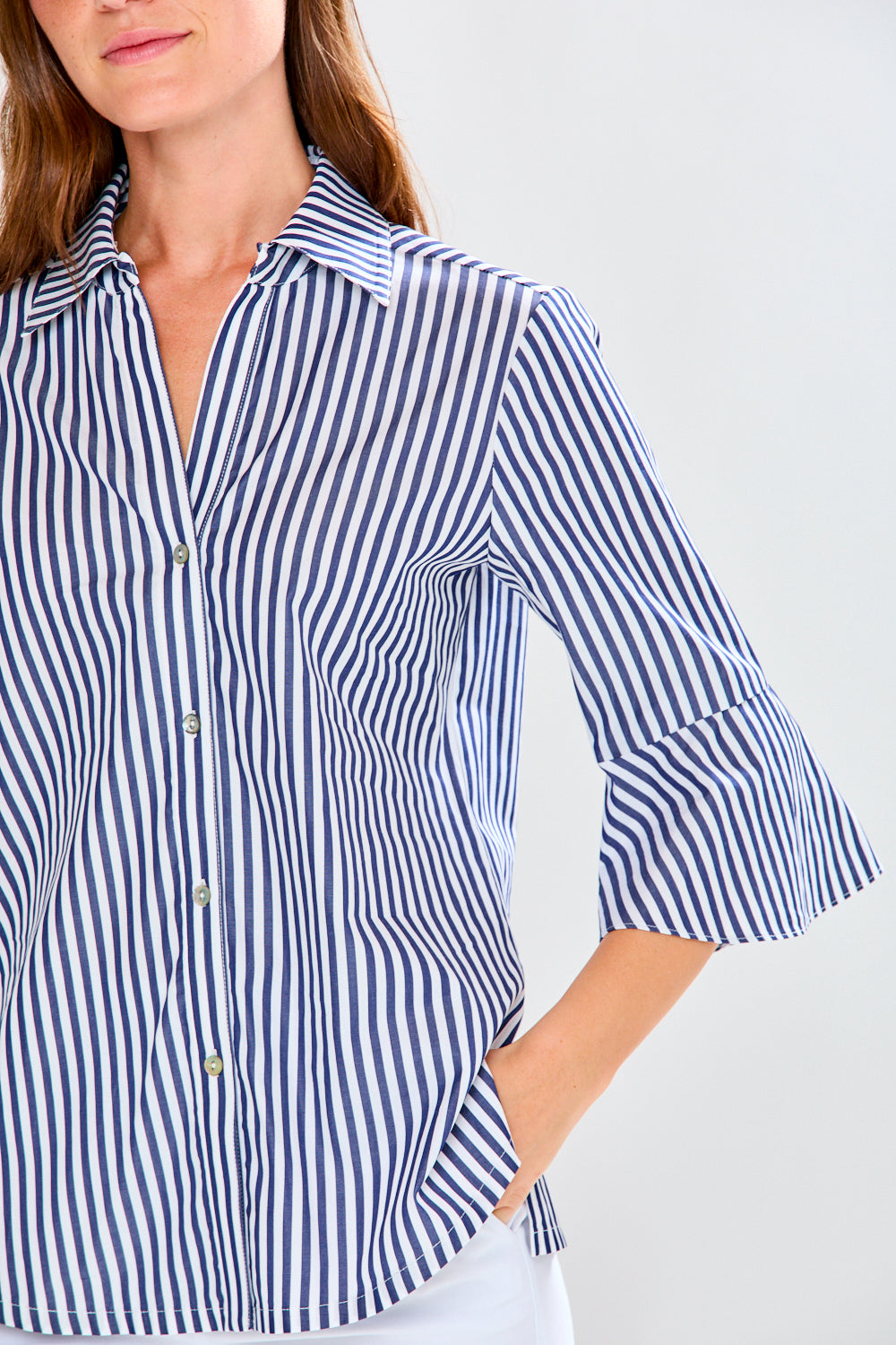 Woman wearing a blue and white striped shirt with rolled-up sleeves on a light gray background