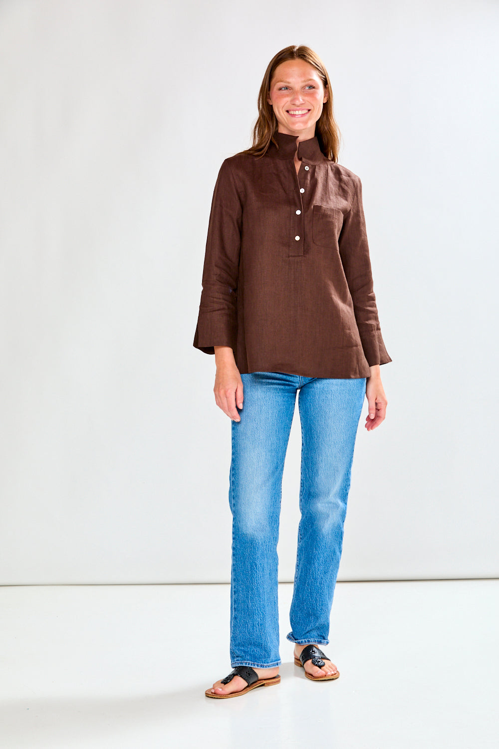 Woman wearing a brown blouse and blue jeans against a white background