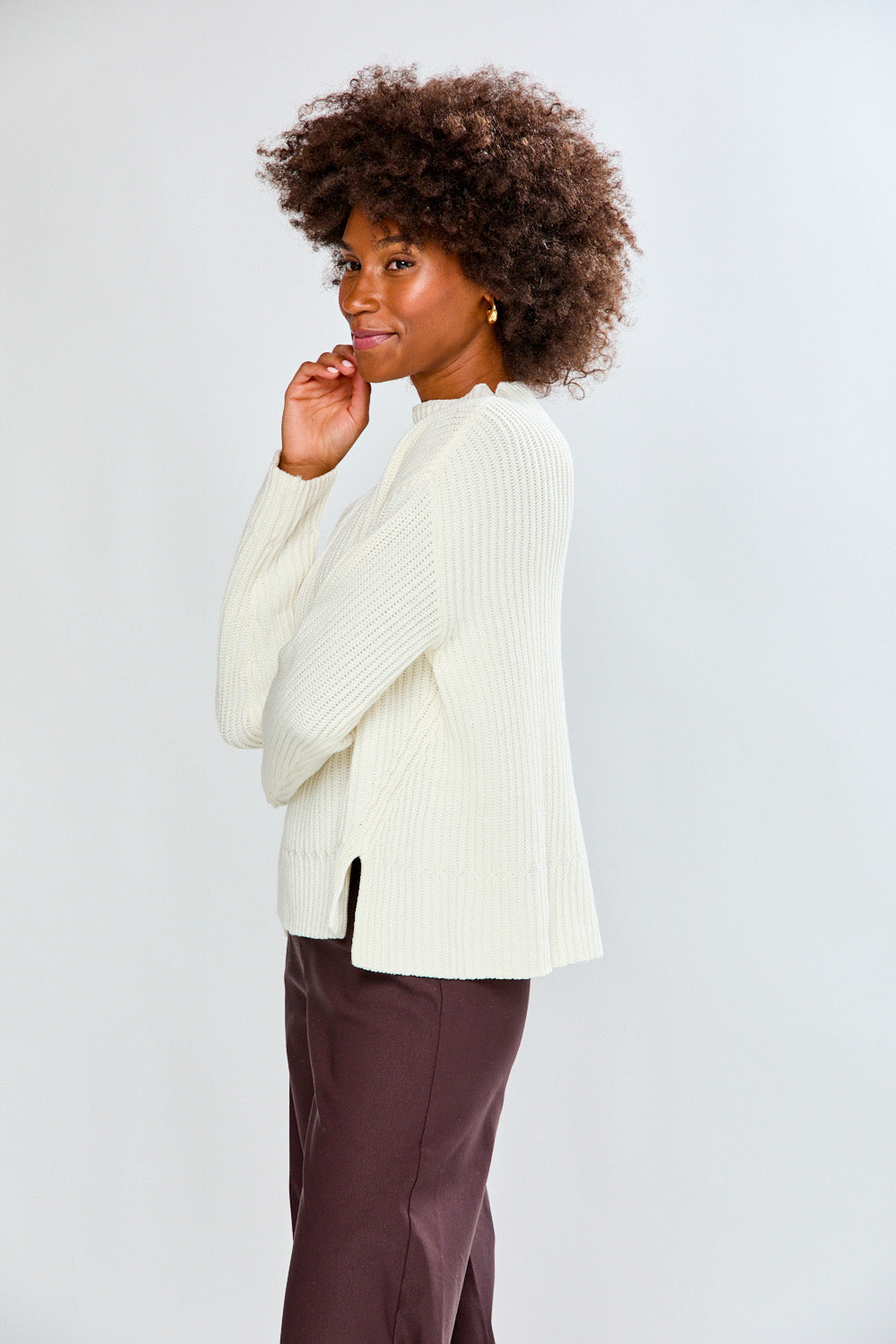 Woman wearing a ivory ribbed sweater and white pants on a plain background