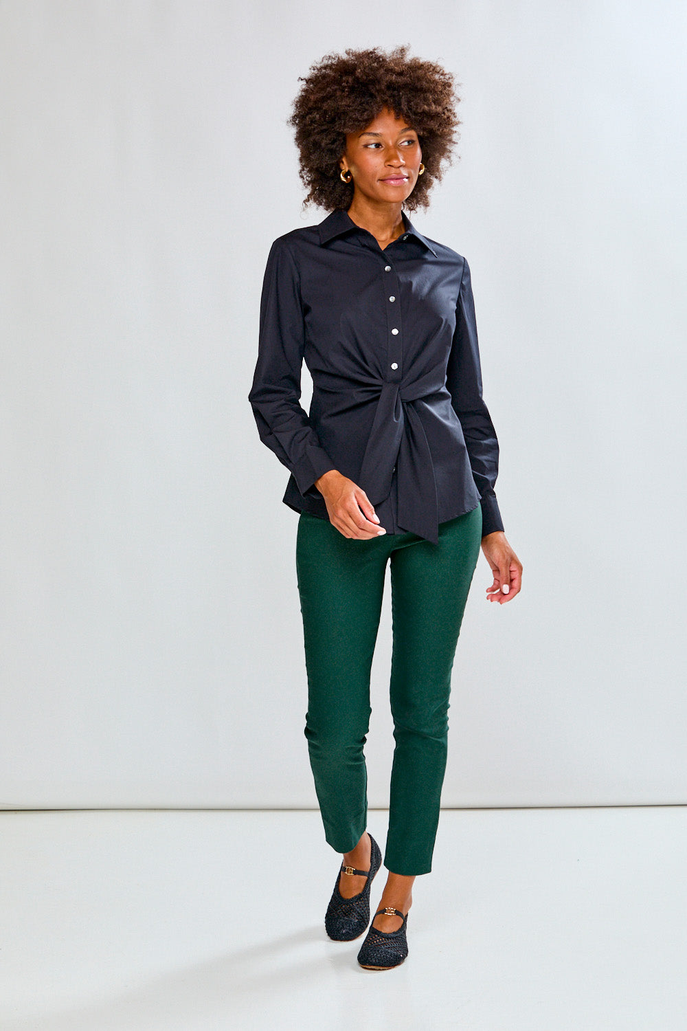 Woman wearing a black shirt and green pants against a white background