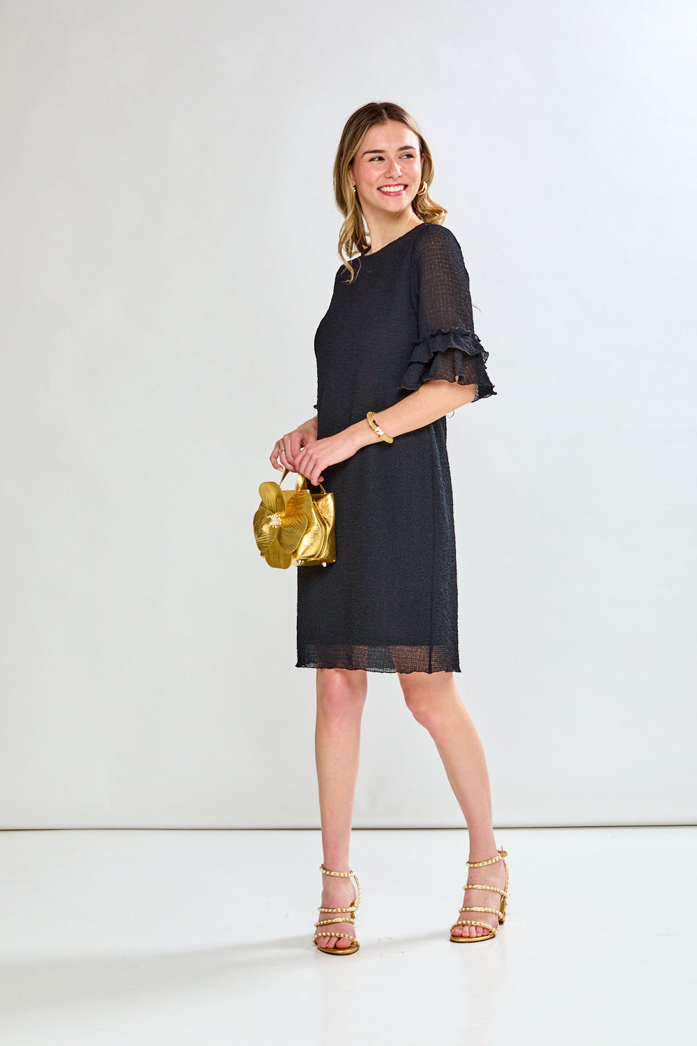 Woman in a black dress holding a gold handbag against a white background