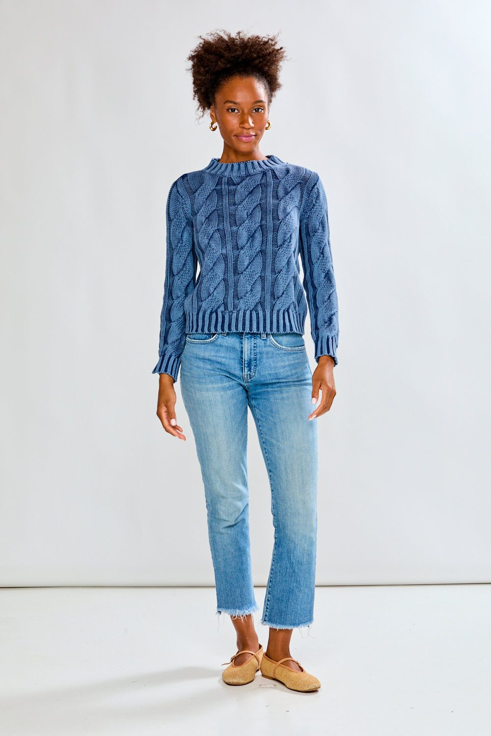 Woman wearing a denim cable knit sweater and blue jeans on a white background