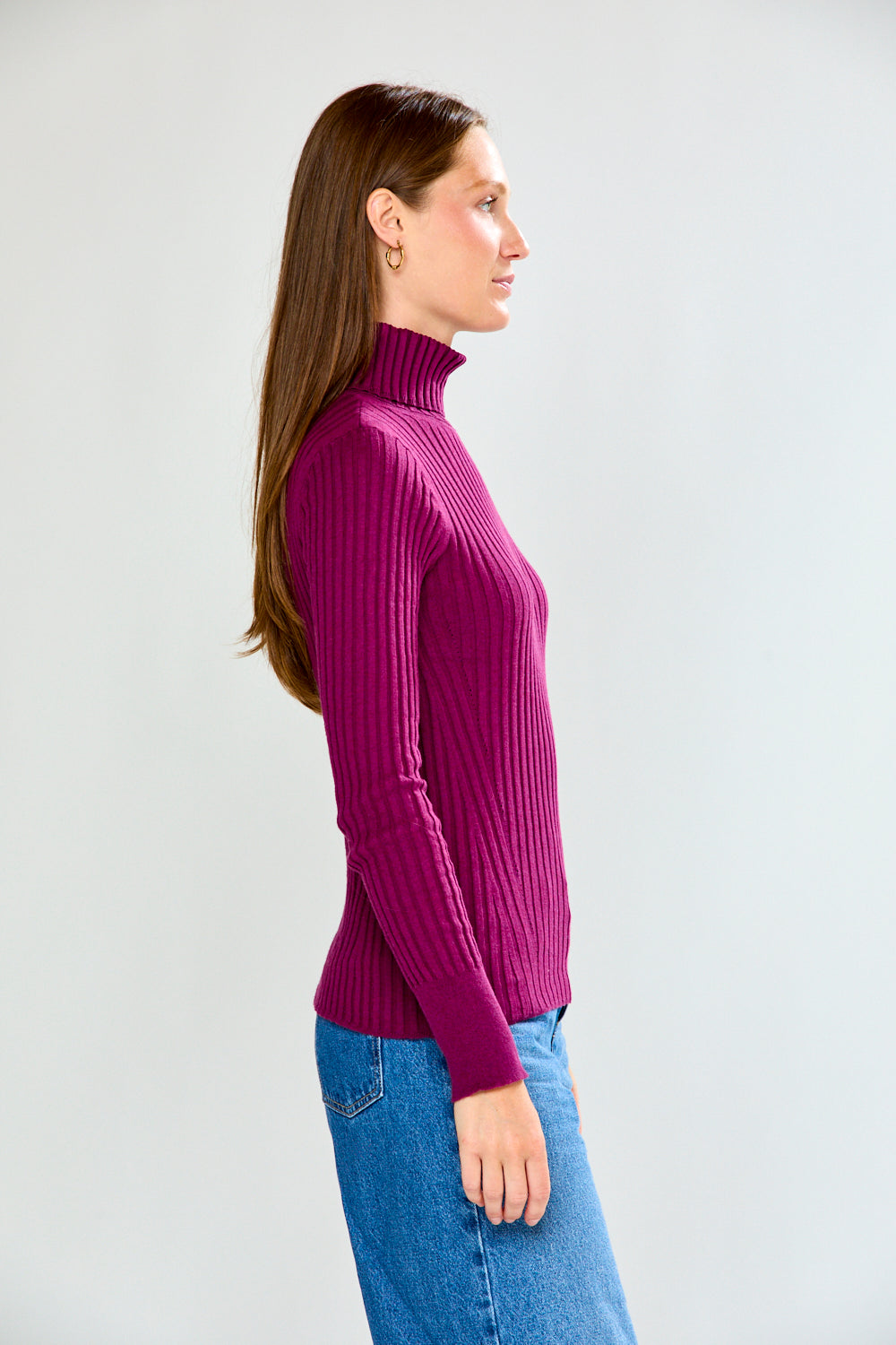 Woman wearing a maroon ribbed turtleneck sweater and blue jeans on a white background