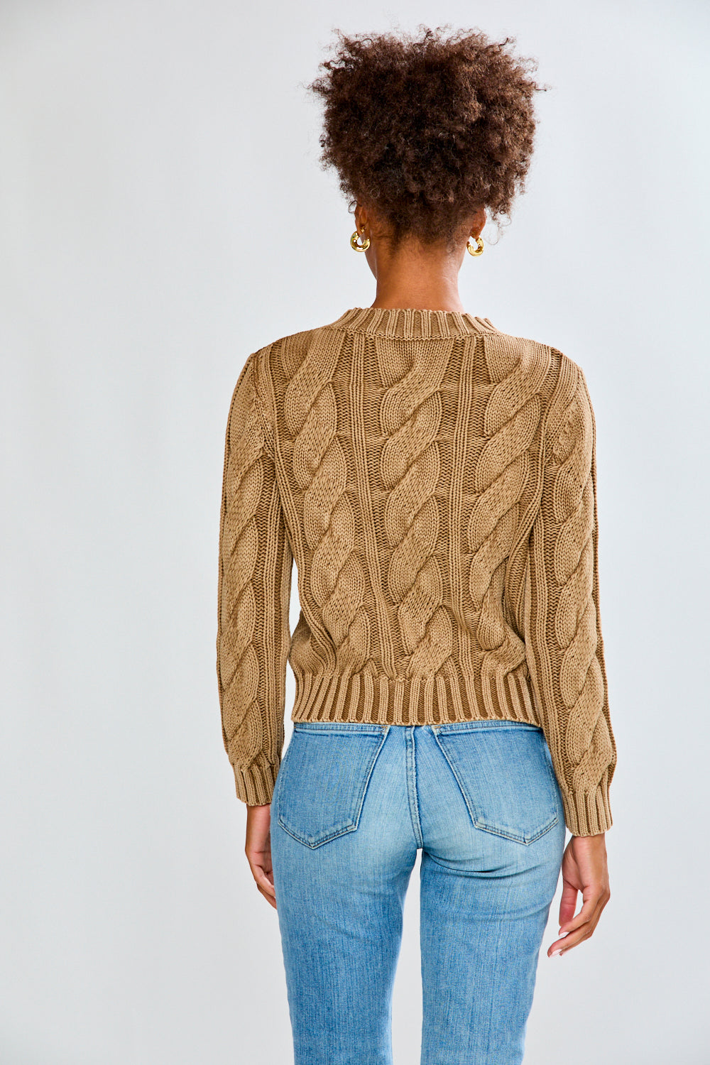 Woman wearing a toffee cable knit sweater and blue jeans on a white background