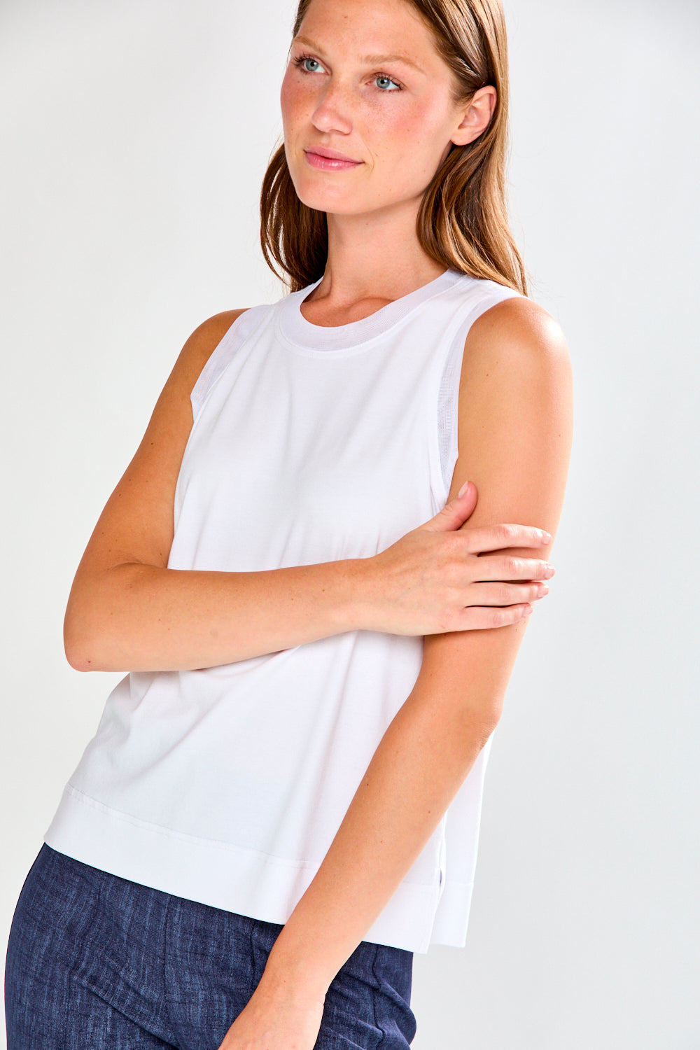 Woman wearing a white sleeveless top against a plain background