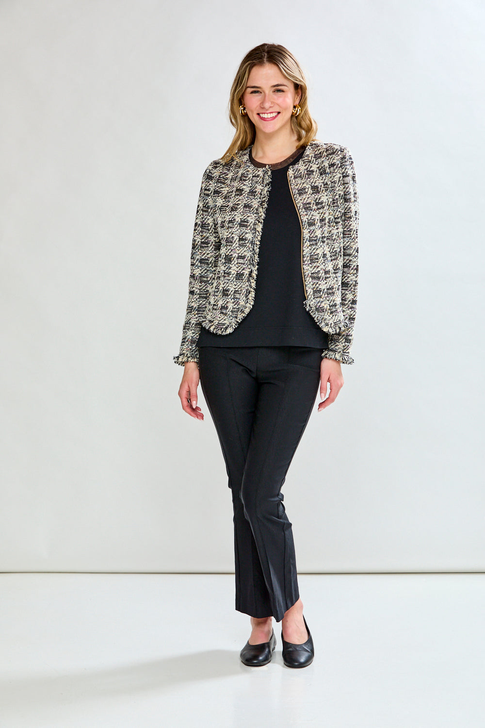Woman wearing a black and white patterned jacket over a black top and pants on a white background