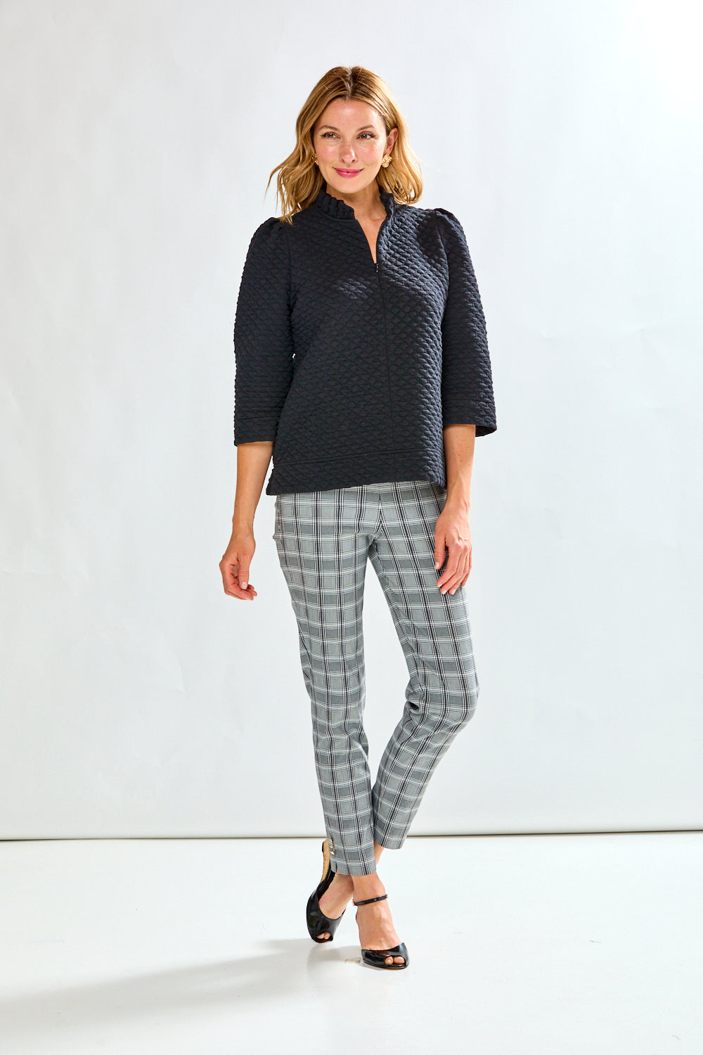 Woman wearing a textured black sweater and plaid pants against a light background