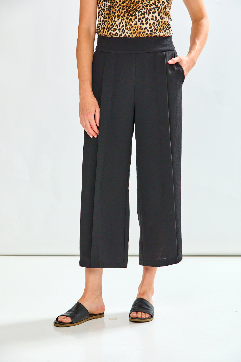 Person wearing black wide-leg pants with a leopard print top on a white background