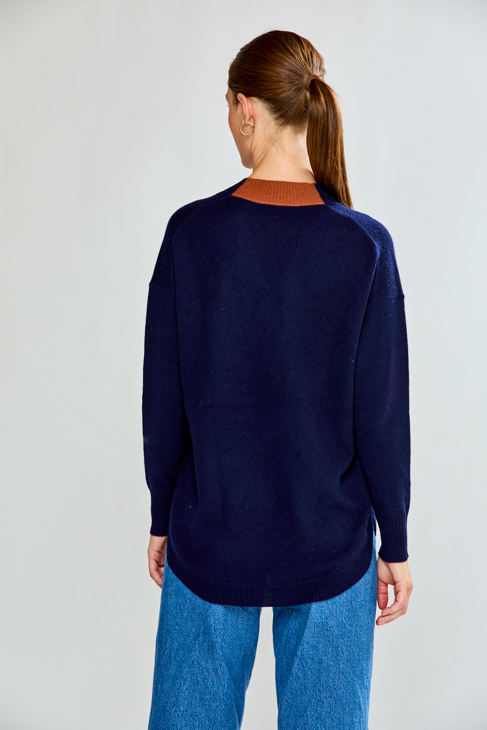 Woman wearing a navy sweater and blue jeans against a plain background