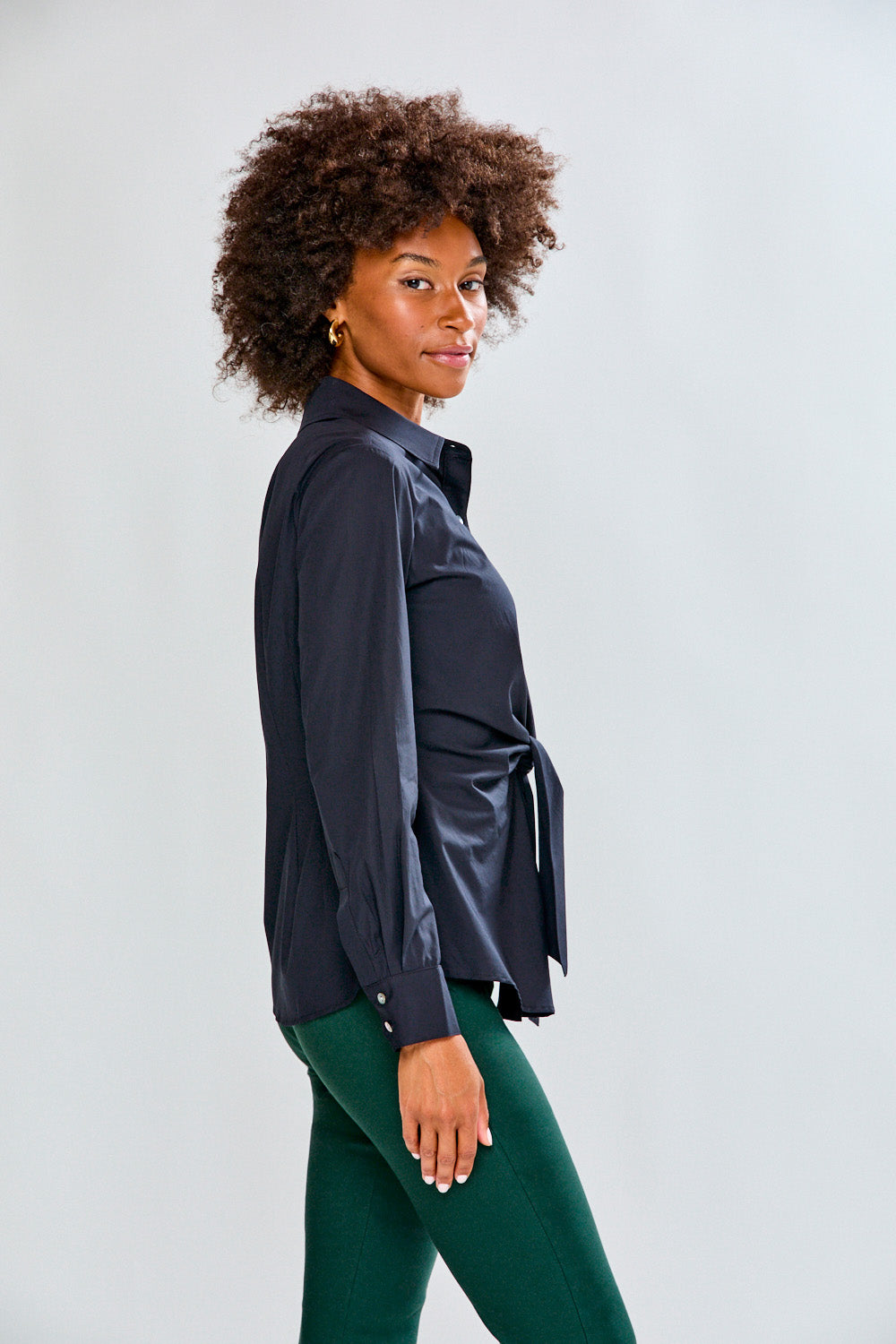 Woman wearing a black shirt and green pants against a plain background