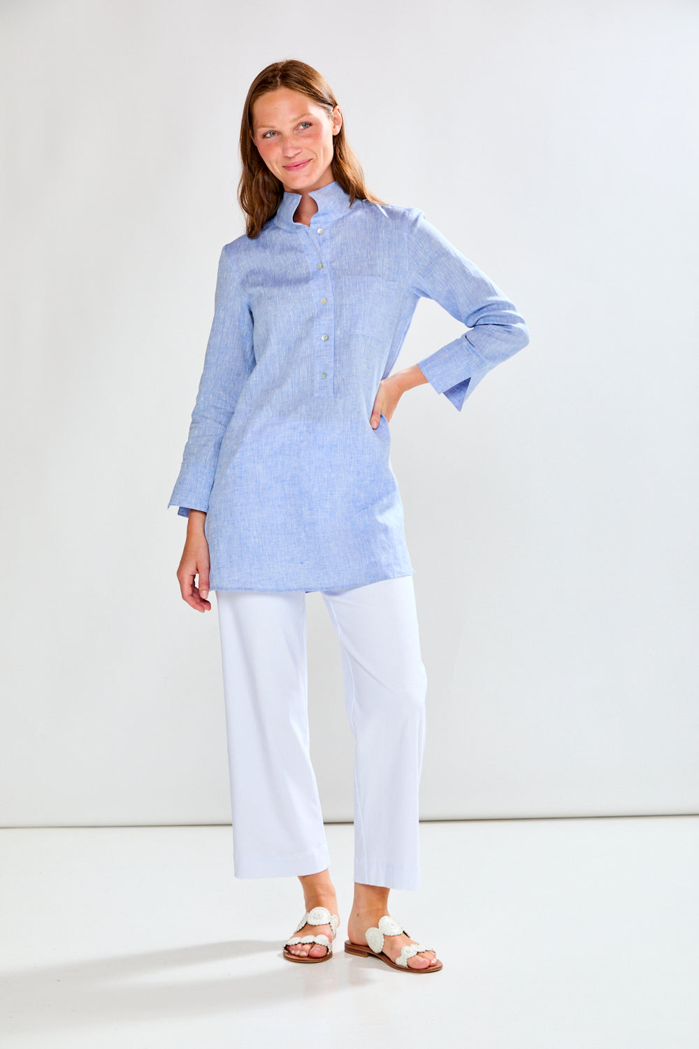 Woman wearing a light blue striped shirt and white pants on a white background