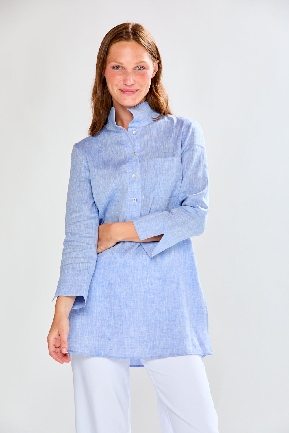 Woman wearing a light blue shirt and white pants on a plain background