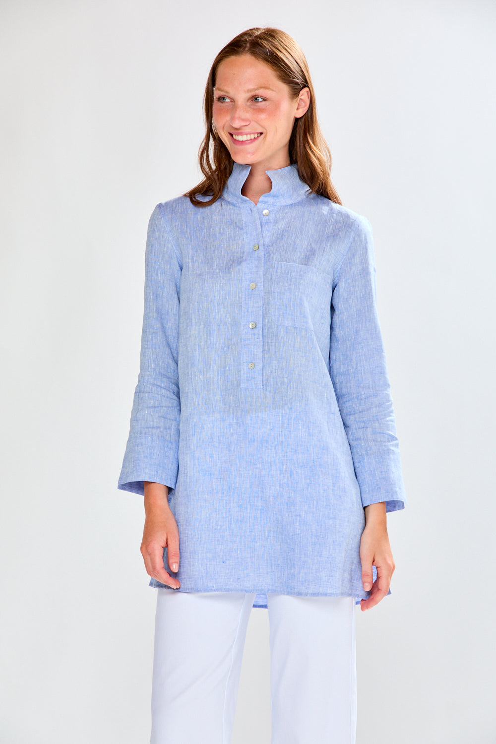 Woman wearing a medium blue shirt and white pants on a plain background
