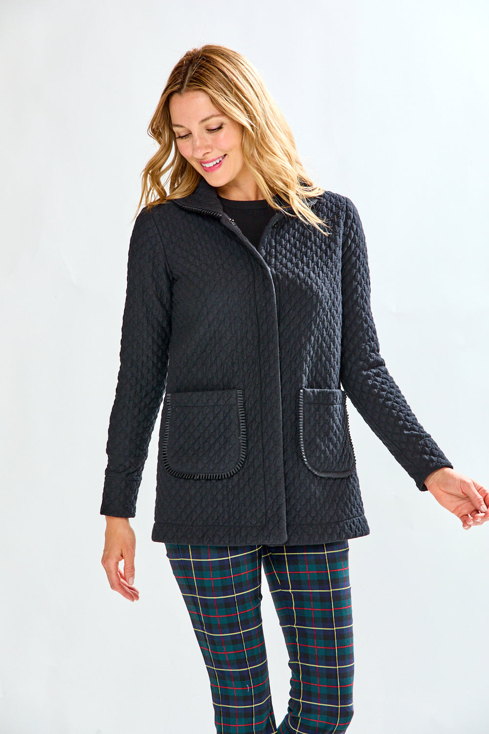 Woman wearing a black quilted jacket and plaid pants on a white background