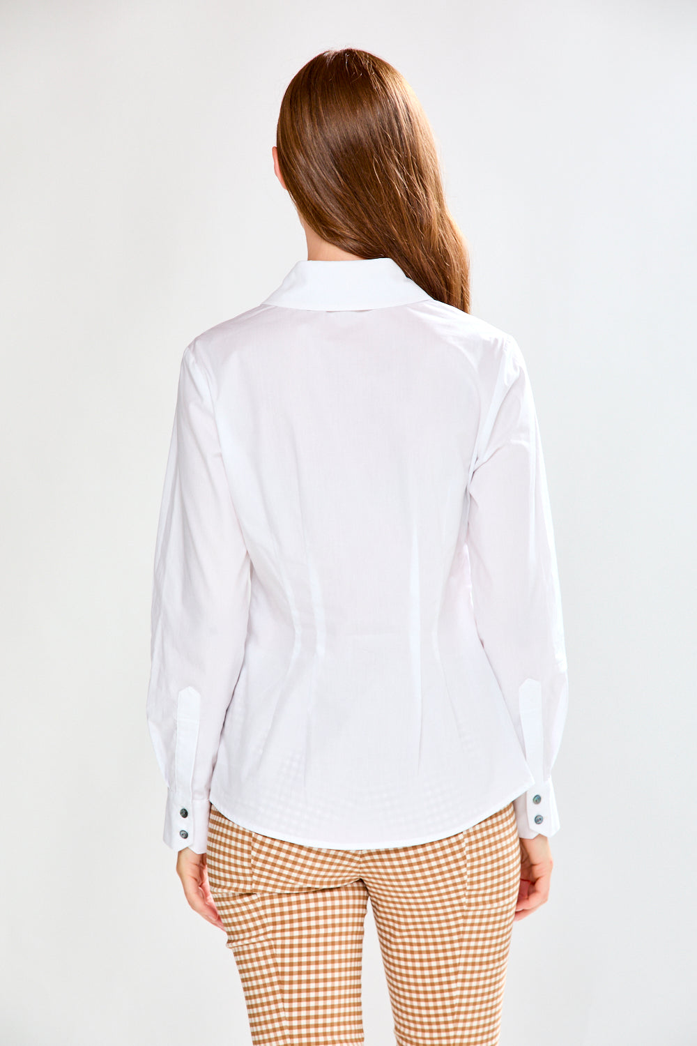 Woman wearing a white shirt with a tie waist and checkered pants on a white background