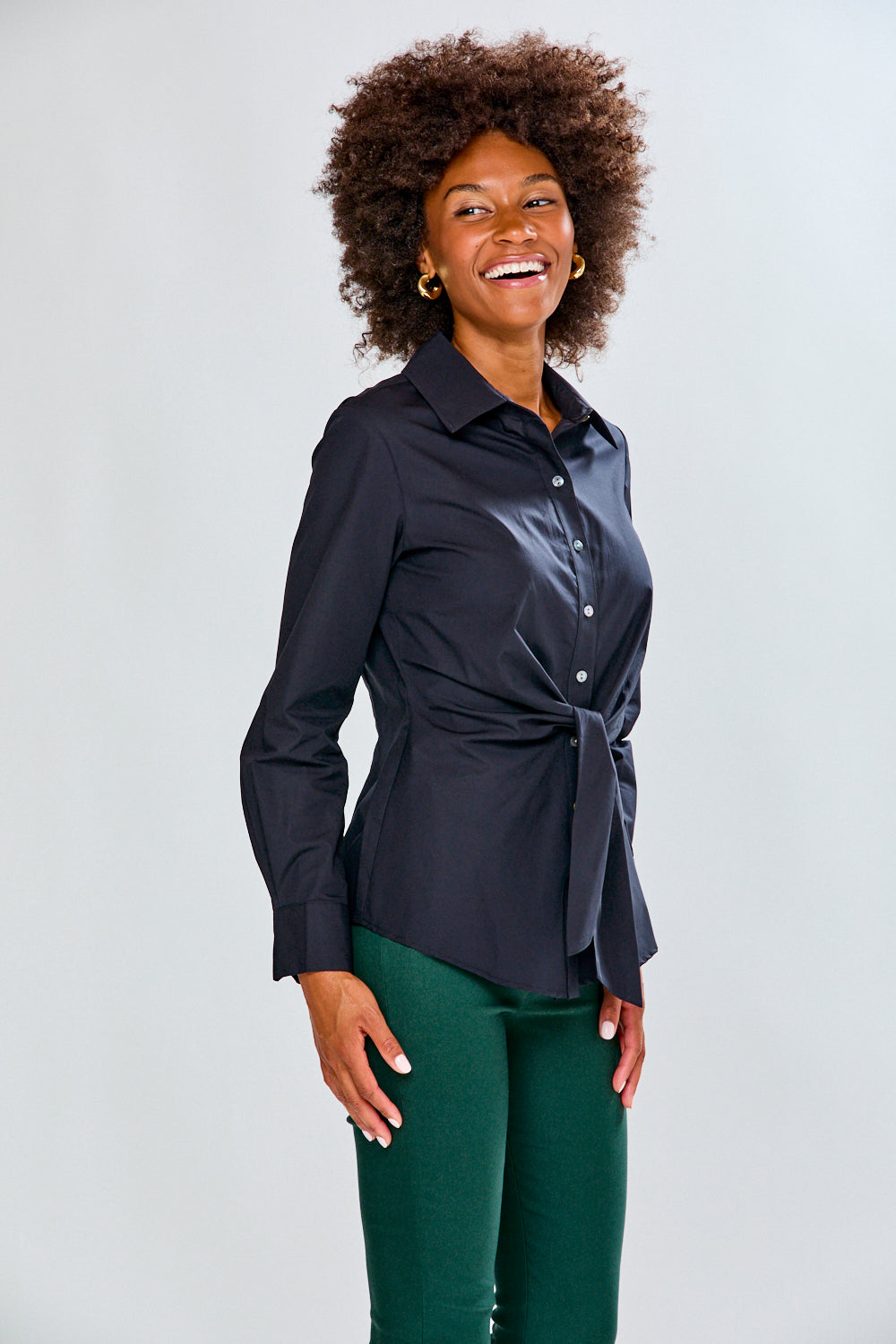 Woman wearing a black shirt with a tie waist and green pants on a white background