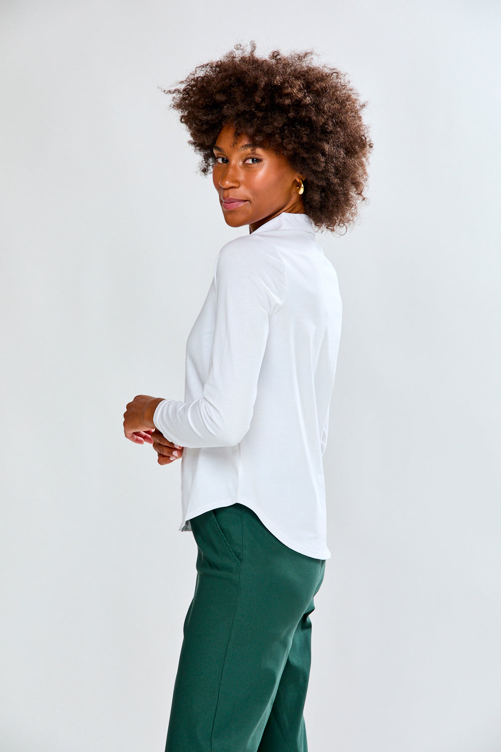 Woman wearing a white shirt and green pants against a plain background