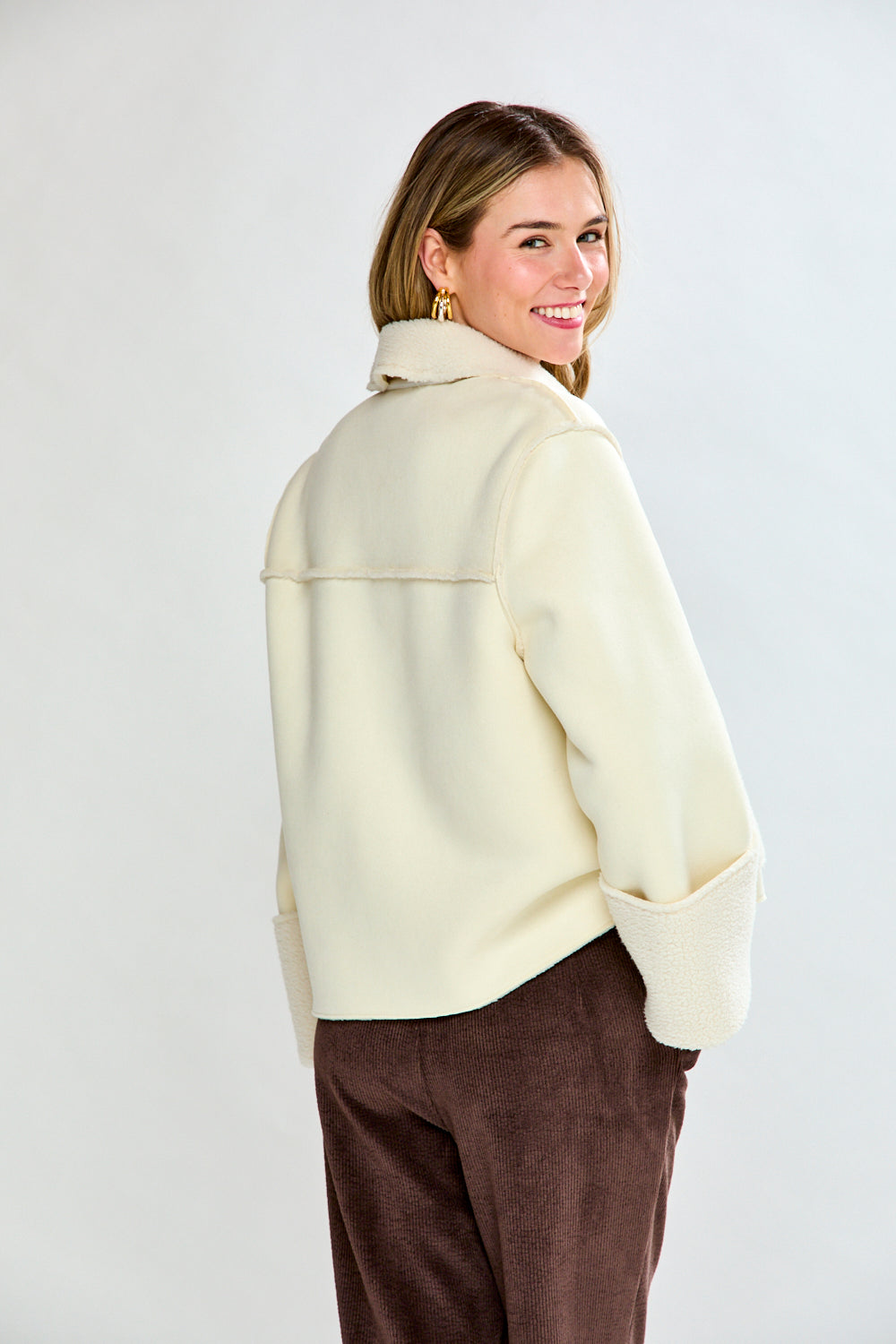 Woman wearing a cream-colored coat over a beige sweater and brown pants on a white background