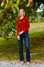 Woman in a red sweater and blue jeans standing outdoors near trees