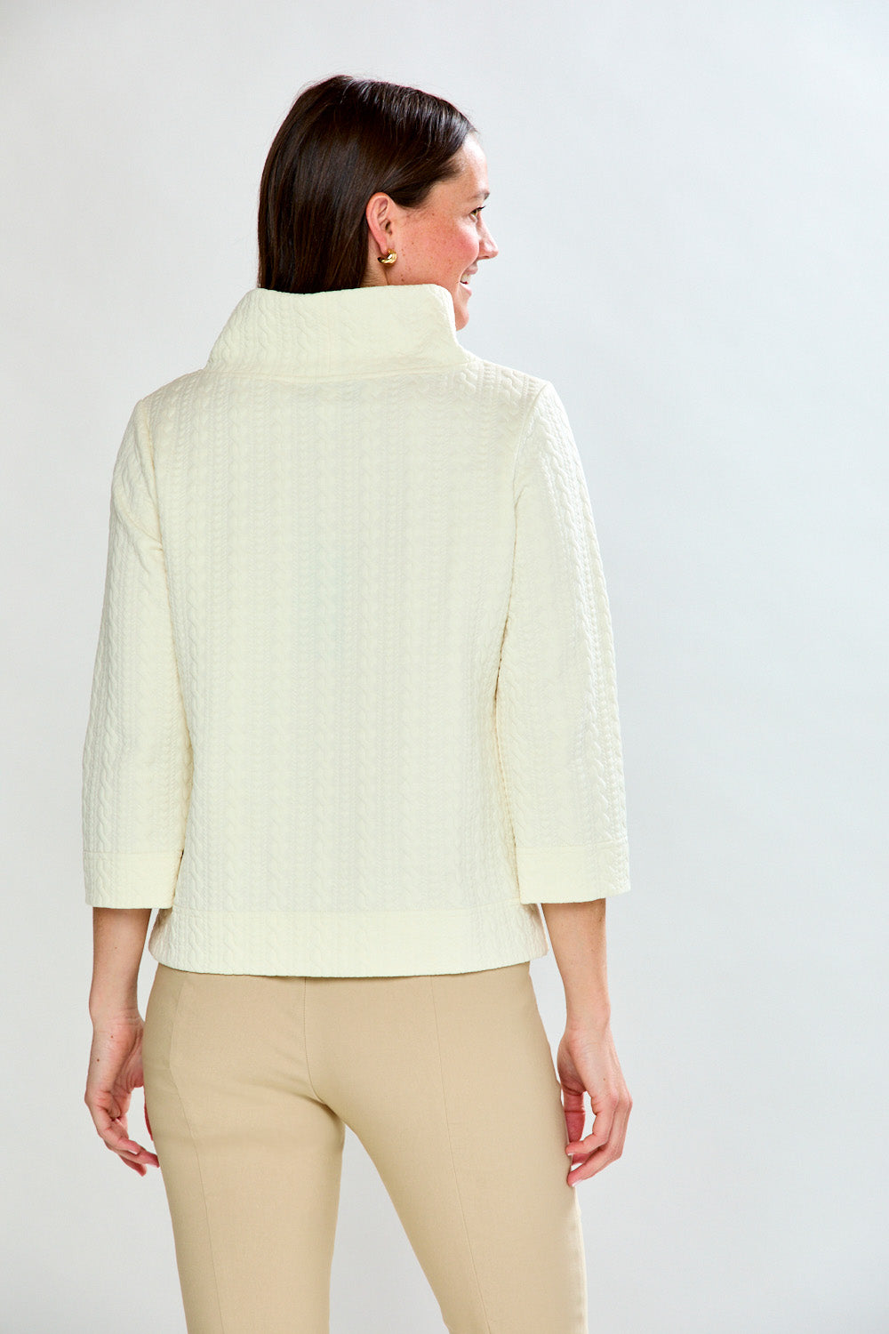 Woman wearing a ivory top and beige pants against a white background
