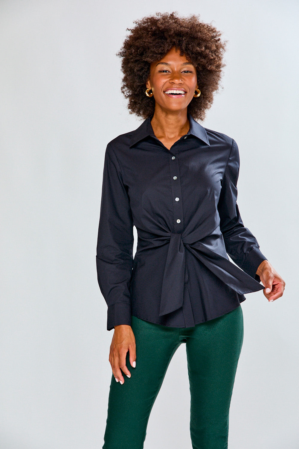 Woman wearing a black blouse with a tie detail on a plain background