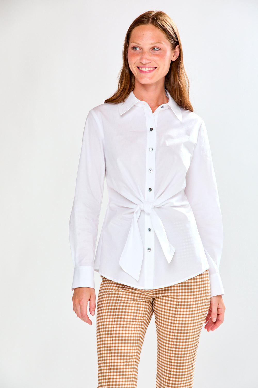 Woman wearing a white shirt with a tie waist and checkered pants on a white background