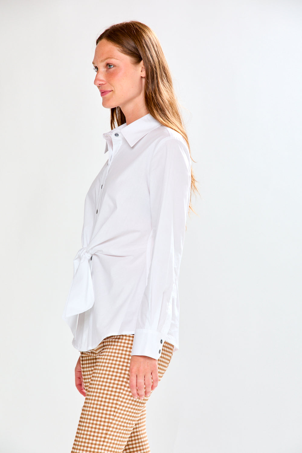 Woman wearing a white shirt with a tie waist and checkered pants on a white background