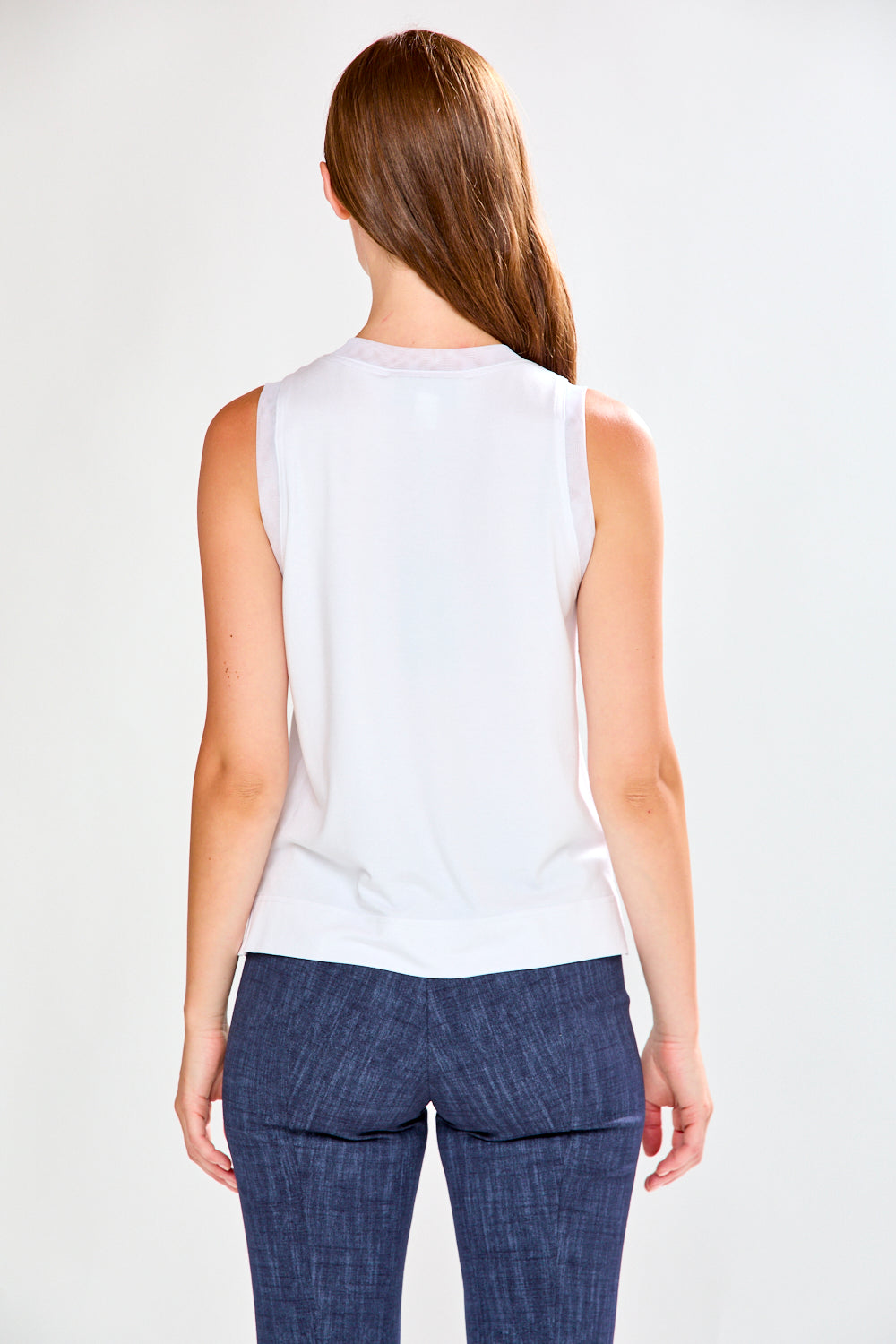 Woman wearing a white sleeveless top and blue pants on a white background
