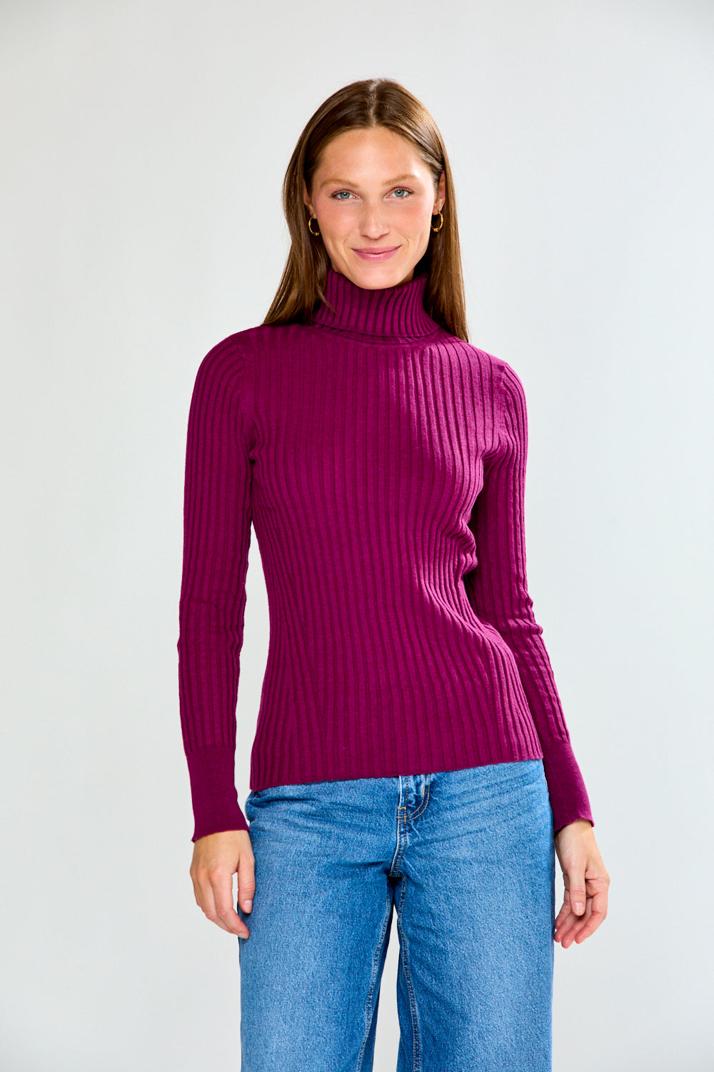 Woman wearing a maroon ribbed turtleneck sweater and blue jeans on a white background