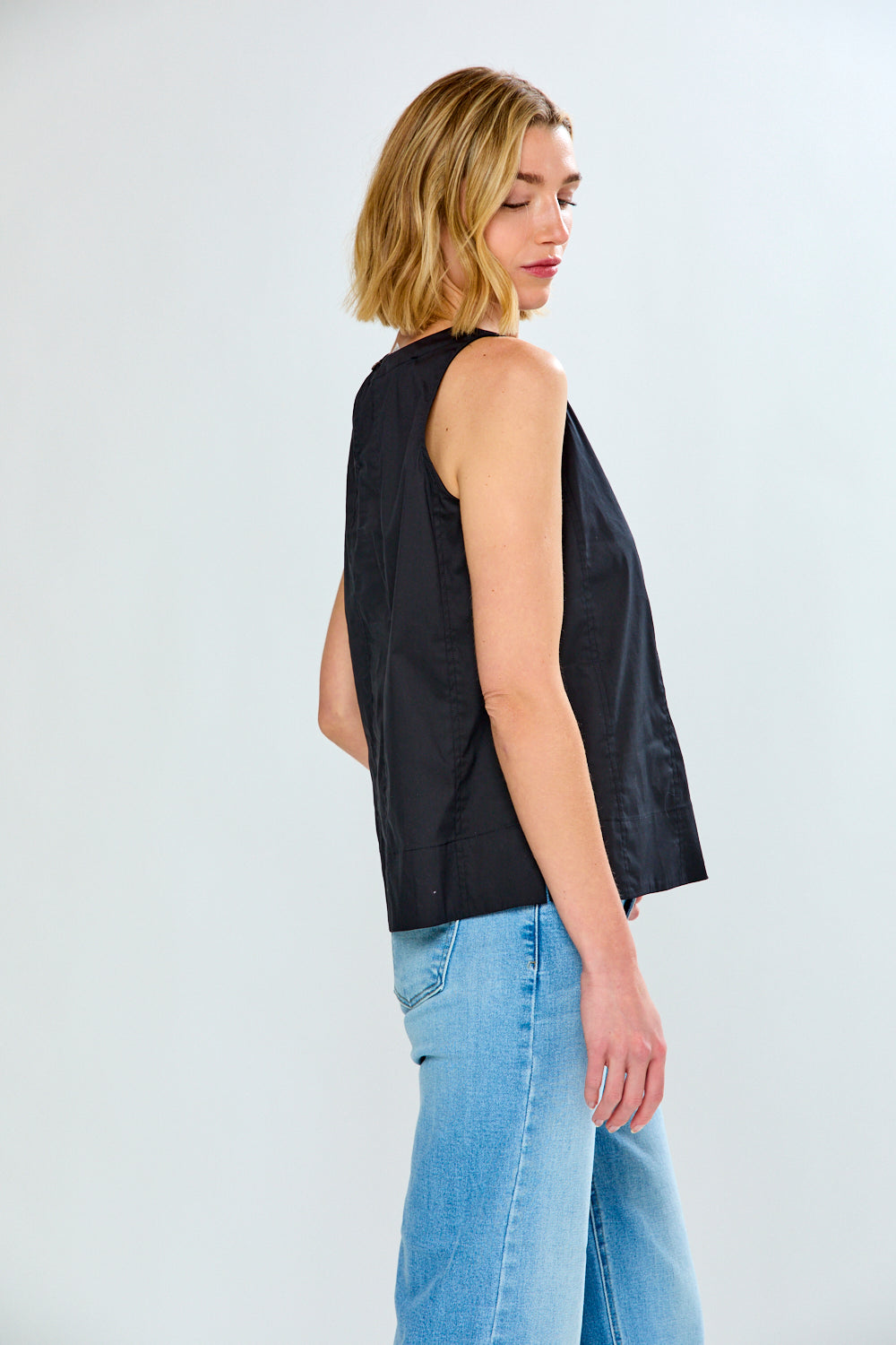 Woman wearing a black sleeveless top and blue jeans on a white background