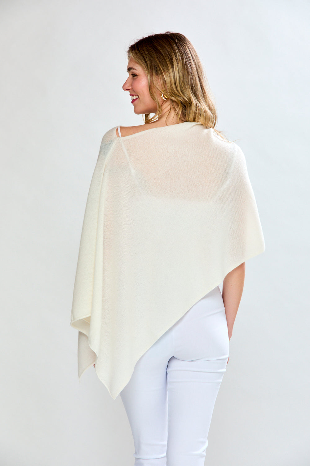 Woman wearing a cream-colored shawl over a white top and pants on a light gray background
