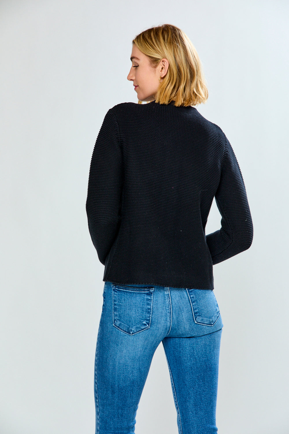 Person wearing a black sweater and blue jeans on a light gray background