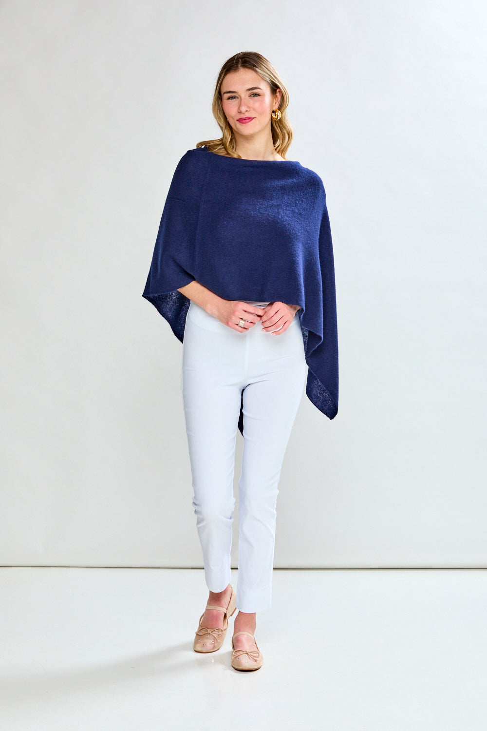 Woman wearing a navy blue poncho over a white top and pants on a white background