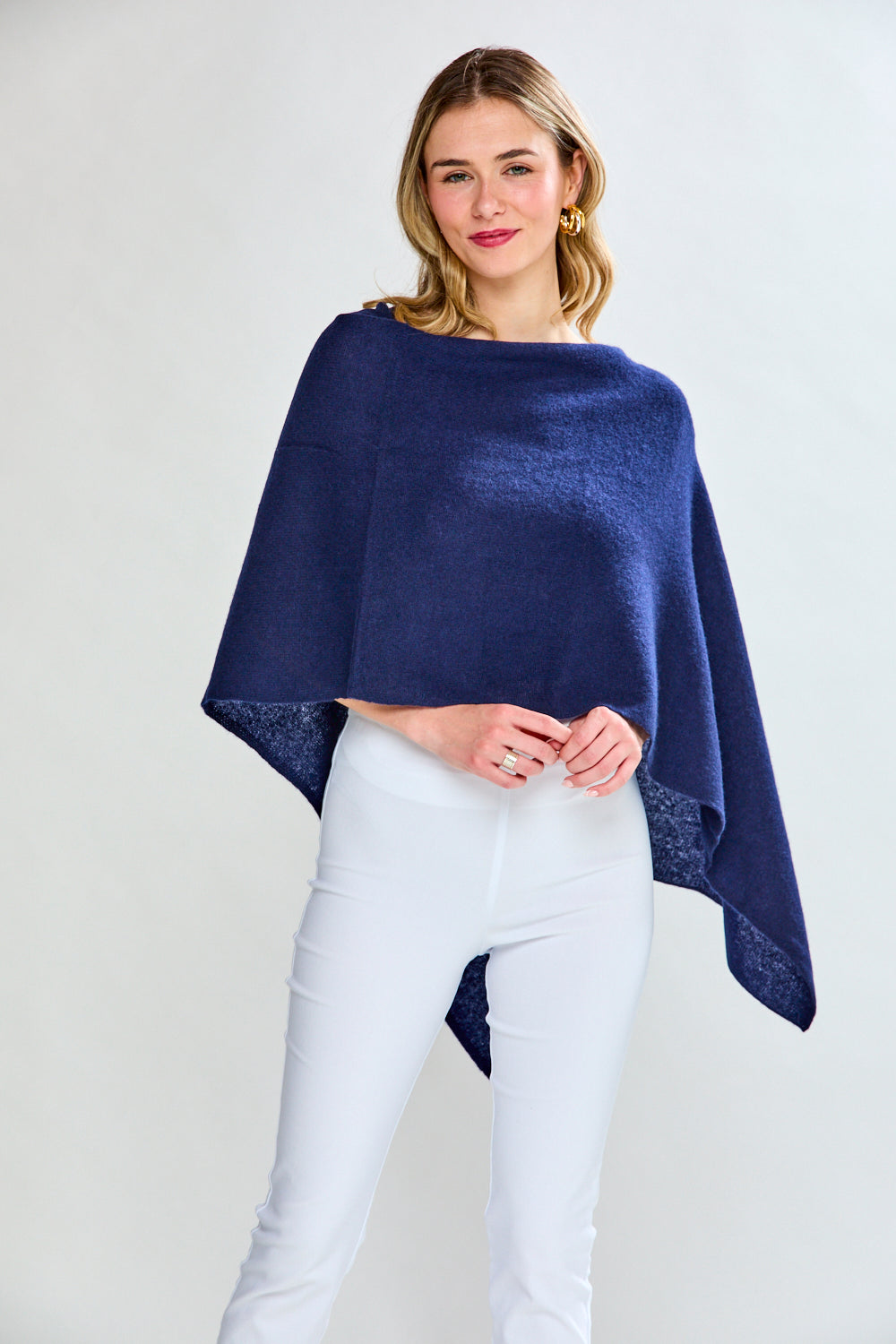 Woman wearing a navy blue poncho over a white outfit on a light gray background