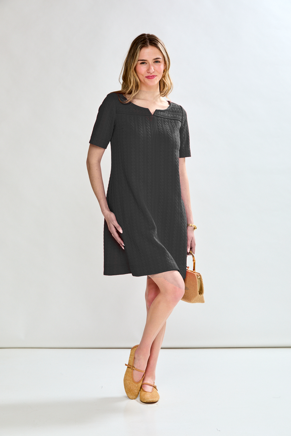 Woman wearing a black dress holding a beige clutch against a white background