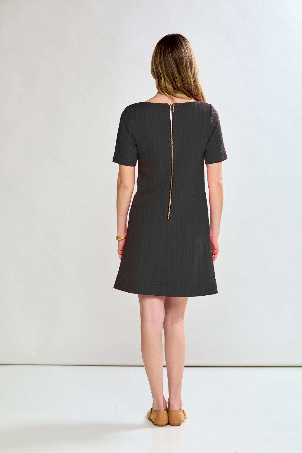 Woman wearing a black dress with a gold zipper on a white background