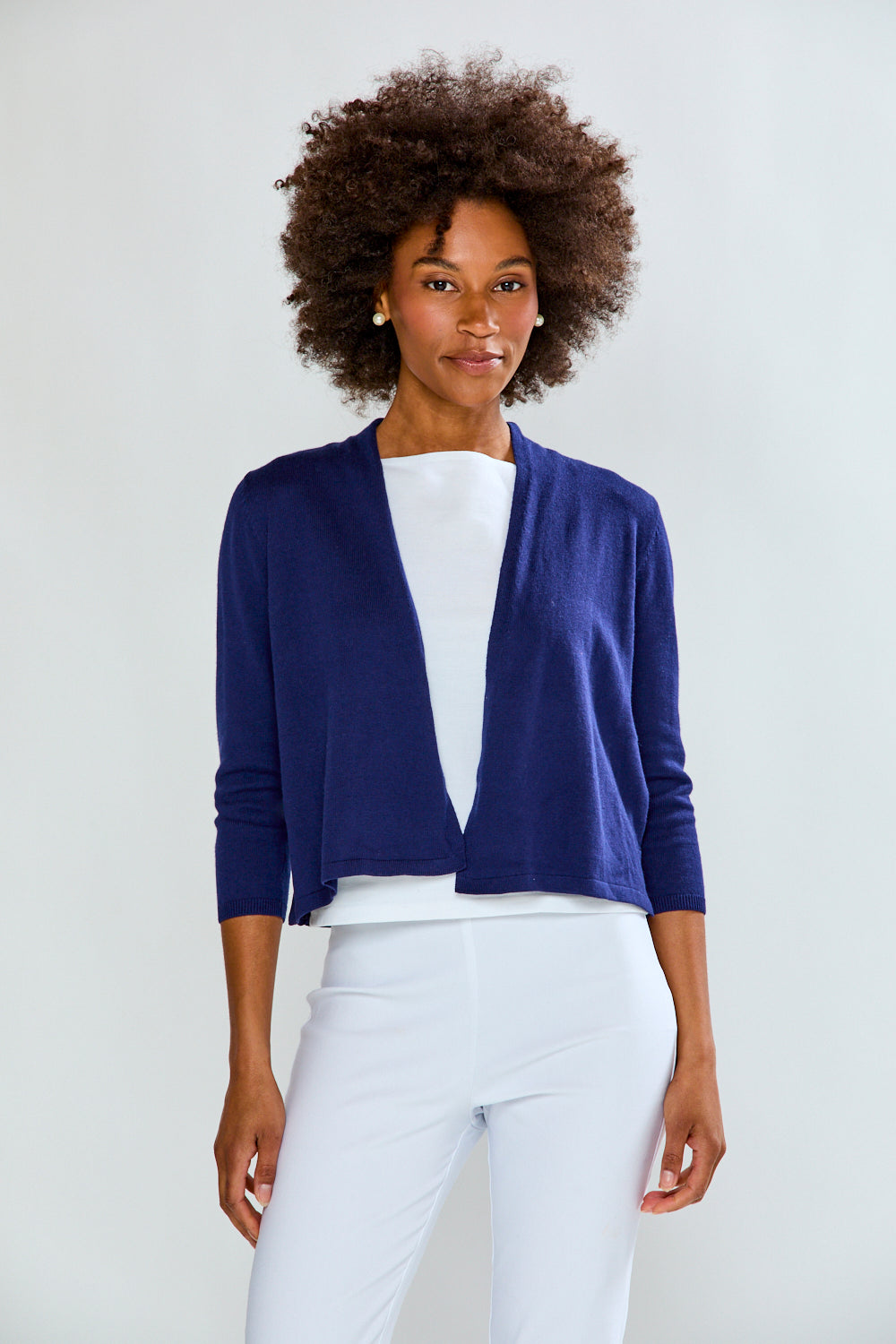 Woman wearing a blue cardigan over a white top and pants on a light gray background